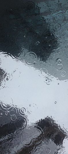 the reflection of clouds in water with raindrops on it's surface is shown