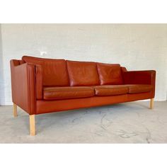 a brown leather couch sitting on top of a cement floor next to a white wall