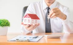 a man is holding a house key and sitting at a desk in front of him