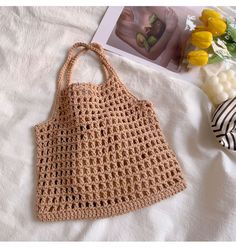 a crocheted bag sitting on top of a bed next to a magazine and flowers