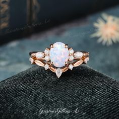 a white opal and diamond ring sitting on top of a black velvet cushioned surface