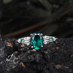 an emerald colored ring sitting on top of a rock with green stones in the middle