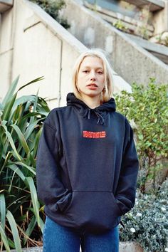 a woman in a black hoodie standing in front of a plant Embroidered Red Hoodie For Streetwear, Red Embroidered Hoodie For Streetwear, Sporty Embroidered Hoodie For Streetwear, Embroidered Black Hoodie For Streetwear, Black Embroidered Hoodie For Streetwear, Red Hoodie With Embroidered Logo For Streetwear, Sleep Embroidery, Stylish Lifestyle, Winter Dress Outfits