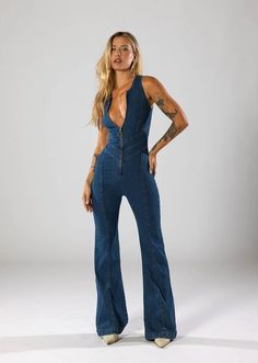 This plunge flare denim jumpsuit is a bold and stylish, combining a vintage-inspired silhouette with a modern edge. The deep neck-line and fitted design accentuate your figure, while the flared length add a touch of retro style. Features: Material: Crafted from high-quality denim that offers durability and a comfortable fit. Design: Features a deep plunge neck-line with a fitted waist, enhancing the overall silhouette and creating a striking look. Fit: The jumpsuit is designed to be form-fitting Jean Jumpsuit Outfit, Revice Denim, Comfy Jumpsuits, Image Svg, Awesome Outfits, Stretch Denim Fabric, Deep Plunge, Plunge Neckline, Fashion Icon