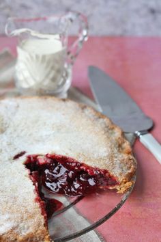 a pie with a slice missing from it on a plate next to a glass pitcher