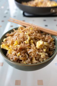 a bowl filled with rice and eggs next to chopsticks on top of a table