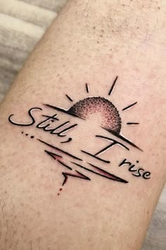 a small tattoo on the leg that says still i rise with an arrow and sun