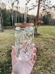 a person holding up a glass jar with writing on it in front of some trees