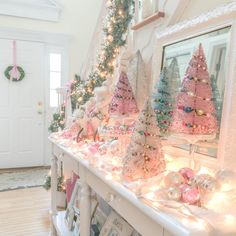 a white mantle topped with christmas trees covered in pink and green ornaments next to a mirror