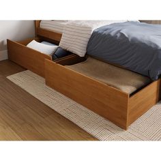 a bed with two drawers underneath it on the floor next to a rug and pillows