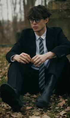 a young man in a suit and tie sitting on the ground with his hands folded