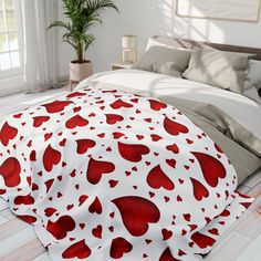 a bed with red hearts on it in a white and gray bedroom, next to a potted plant