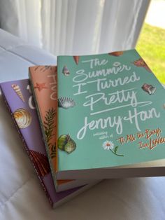 three books sitting on top of a bed next to each other in front of a window