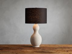 a white vase with a black shade on it sitting on a wooden table next to a gray wall