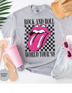 Rock on with our Kiss of Vintage Rock Tee: Tour '88! This edgy t-shirt features a bold pink kiss mouth design on the front, adding a touch of rock and roll flair to your wardrobe. With its vintage vibe and cool "Tour '88" print, this tee is perfect for music lovers and trendsetters alike. Made from high-quality cotton for maximum comfort and durability, it's the ultimate statement piece for any rock-inspired outfit. Get ready to turn heads and rock out in style with this must-have tee! *Unisex Sizing* Summer Rock T-shirt With Band Logo, Summer Rock Style T-shirt For Streetwear, Rock And Roll T-shirt With Band Logo For Summer, Rock Style Graphic Print T-shirt For Summer, Rock And Roll Style T-shirt For Summer Streetwear, Trendy Band Logo T-shirt For Summer, Rock Style T-shirt For Summer Concerts, Rock And Roll Band Logo T-shirt For Summer, Rock Style Graphic T-shirt For Spring