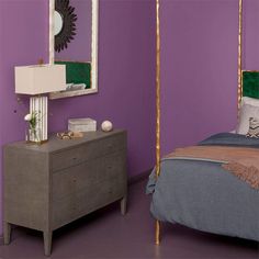 a bedroom with purple walls and a gold frame mirror on the wall next to a bed