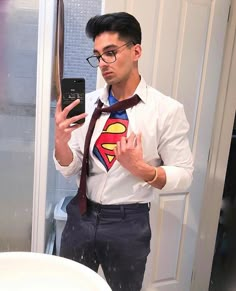 a man wearing a superman shirt and tie while holding a cell phone in his hand