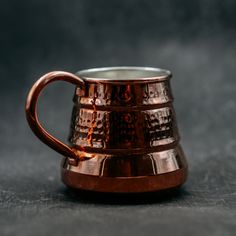 a copper colored mug sitting on top of a gray tablecloth covered floor next to a black wall