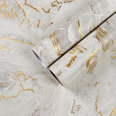 two rolls of white and gold wallpaper on top of each other, one rolled up to the side