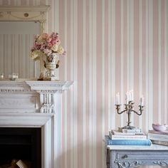 a room with striped wallpaper, a fireplace and a vase filled with flowers on top of books