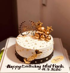 a white cake with gold decorations on top and happy birthday written on the front side