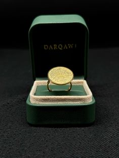 a gold ring in a green box on a black surface with the word darquaw written across it