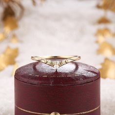 a gold wedding ring sitting on top of a red wooden box with snow around it