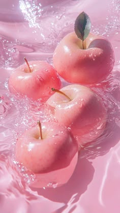 three pink apples floating in water with a green leaf