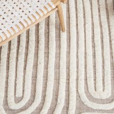 a white and brown area rug on top of a wooden table next to a wicker chair