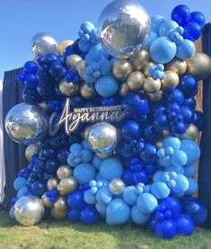 blue and gold balloon arch with happy birthday sign on it in front of a wooden fence