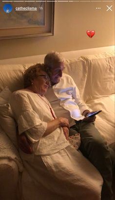 an older man and woman sitting on a couch looking at a tablet computer screen with the caption i love you