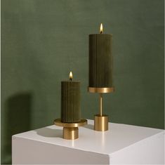 two gold candles sitting on top of a white table next to each other in front of a green wall