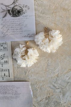 two white flower earrings sitting on top of an old sheet of paper next to music sheets