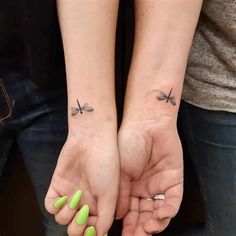 two people holding hands with small tattoos on their arms and one has a green manicure