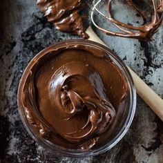 a bowl filled with chocolate frosting next to a wooden spoon and whisk