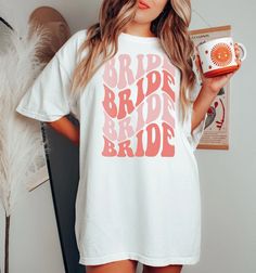 a woman wearing a merry and pregnant t - shirt holding a cup in her hand