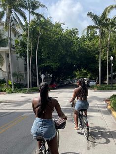 two women riding bikes down the street with palm trees in the backgrouds