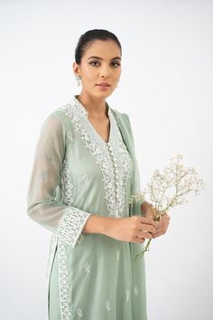 Introducing a charming ensemble featuring a basil green cotton net shirt, delicately hand embroidered and adorned with resham and French knot work. The intricate detailing adds a touch of elegance to the overall design. The shirt is paired with loose-fitting pants in a matching shade, featuring similar resham work on the bottoms, creating a cohesive look. To complete the ensemble, a handworked chiffon dupatta with lace edging is included, providing a graceful finishing touch. Lily Of The Nile, Net Shirt, Resham Work, Loose Fitting Pants, Fitting Pants, The Nile, Chiffon Dupatta, French Knot, Lace Edging