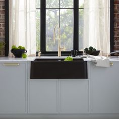 a kitchen sink sitting under a window next to a counter top with fruit on it