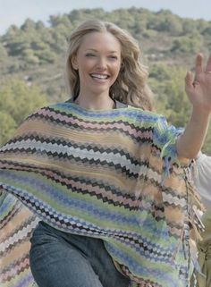 a woman is smiling and waving with her hand in the air while wearing a multicolored ponchy