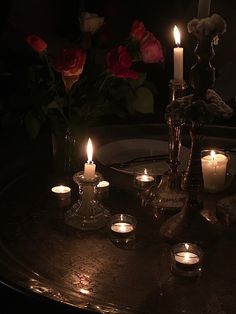 candles are lit on a table with roses in the background