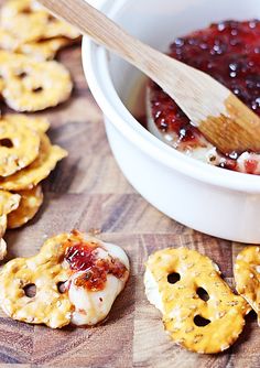 some crackers and jelly in a bowl with a wooden spoon next to them on a table