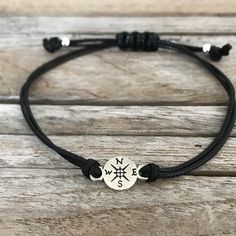 a black cord bracelet with an anchor and compass charm on the end, sitting on a wooden surface