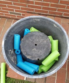 a bucket filled with blue and green items on top of a brick floor next to a sidewalk