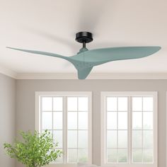 a ceiling fan in a living room with two windows and a plant on the table