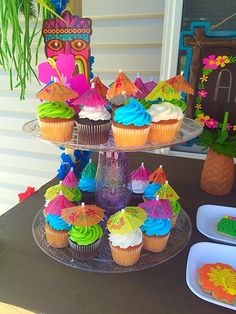 cupcakes on a cake stand decorated with colorful icing and decorations for a birthday party