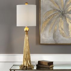 a table with a lamp on it next to a book and a framed painting in the background