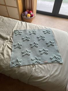 a crocheted blanket sitting on top of a bed next to a basket of fruit