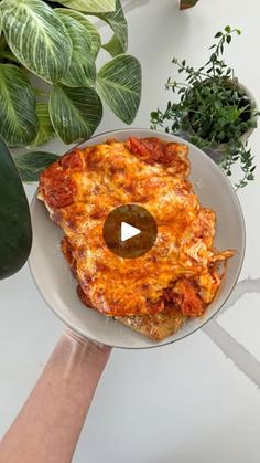 a person holding a plate with pizza on it next to some plants and potted plants