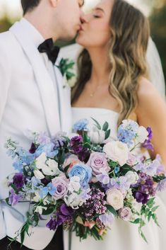 a bride and groom kissing each other in front of the camera with their wedding bouquet